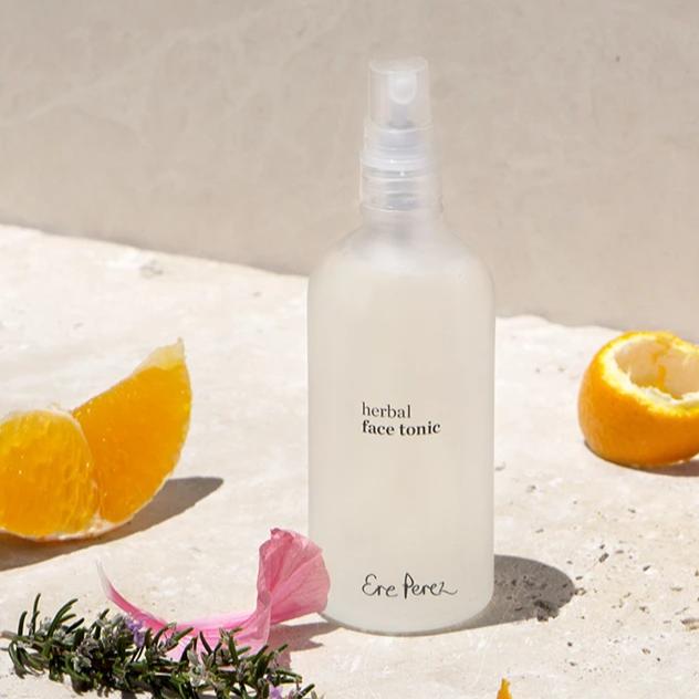 Bottle of Ere Perez Herbal Face Tonic with slices of mandarin orange, rose petal and rosemary sprig.