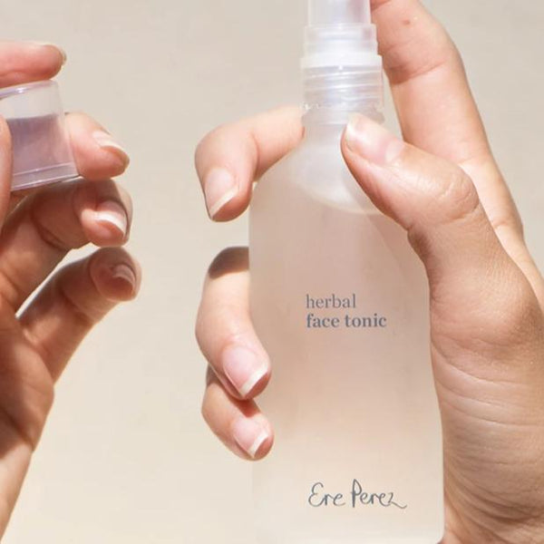 Two hands holding and spraying a bottle of Ere Perez Herbal Face Tonic
