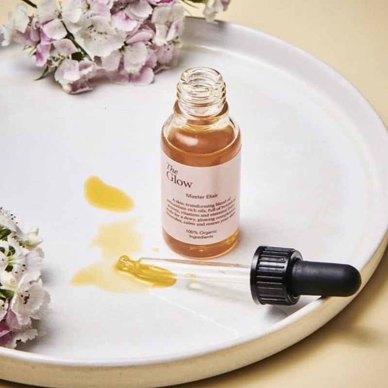 The Glow Master Elixir open bottle on tray with flowers